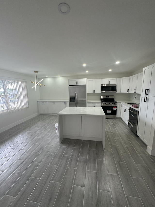 kitchen featuring appliances with stainless steel finishes, a kitchen island, sink, a chandelier, and white cabinetry