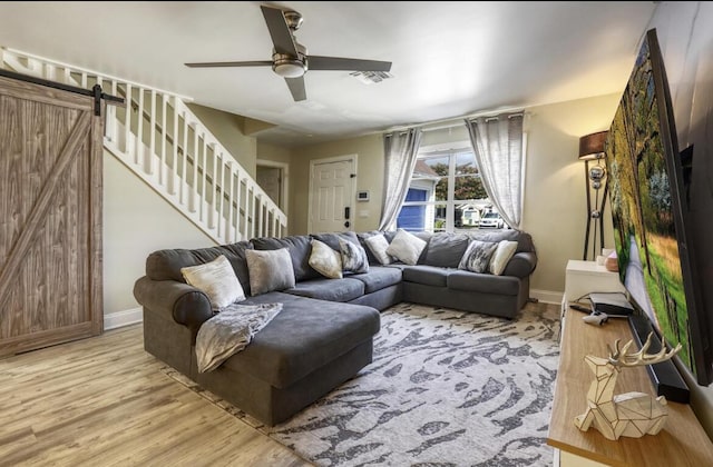 living room with ceiling fan, a barn door, light wood-style flooring, visible vents, and stairway