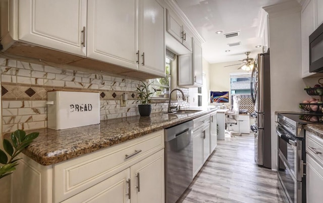 kitchen featuring appliances with stainless steel finishes, dark stone counters, white cabinets, and a sink