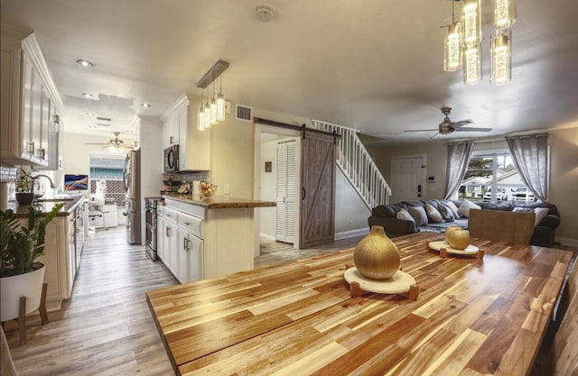 kitchen with a barn door, ceiling fan with notable chandelier, stainless steel appliances, white cabinets, and light wood-type flooring