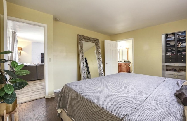 bedroom with connected bathroom, baseboards, and wood finished floors