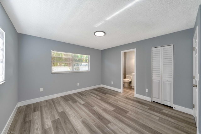 unfurnished bedroom with ensuite bathroom, light wood-type flooring, a closet, and a textured ceiling