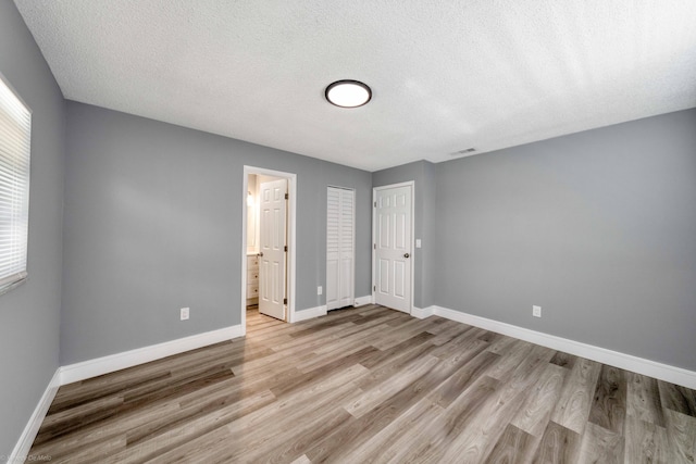 unfurnished bedroom with ensuite bathroom, a textured ceiling, and light hardwood / wood-style flooring