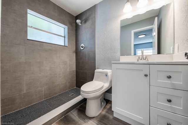 bathroom with toilet, hardwood / wood-style flooring, a textured ceiling, tiled shower, and vanity