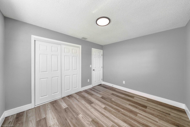 unfurnished bedroom featuring a closet, a textured ceiling, and light hardwood / wood-style flooring