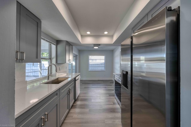 kitchen with a raised ceiling, gray cabinetry, stainless steel appliances, dark hardwood / wood-style floors, and sink