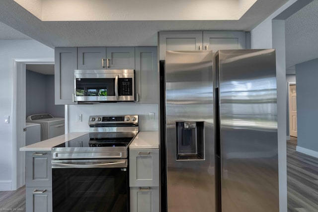 kitchen with stainless steel appliances, washer and dryer, light hardwood / wood-style flooring, and gray cabinetry