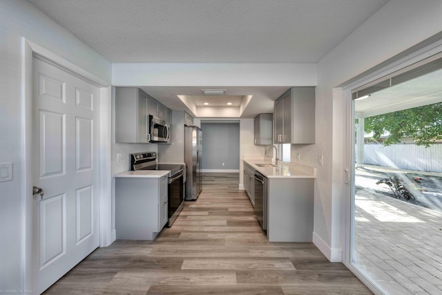 kitchen featuring sink, a raised ceiling, light wood-type flooring, gray cabinetry, and appliances with stainless steel finishes