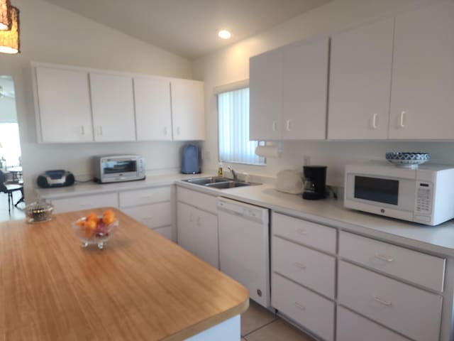 kitchen with lofted ceiling, white appliances, sink, light tile patterned floors, and white cabinetry