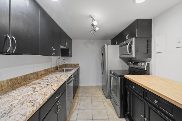 kitchen featuring stainless steel appliances, track lighting, light stone countertops, light tile patterned floors, and sink