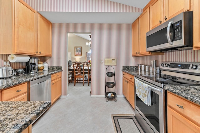 kitchen featuring light tile patterned floors, stainless steel appliances, dark stone countertops, and a chandelier