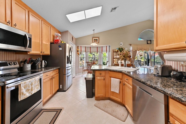 kitchen featuring appliances with stainless steel finishes, light tile patterned flooring, dark stone countertops, vaulted ceiling with skylight, and hanging light fixtures