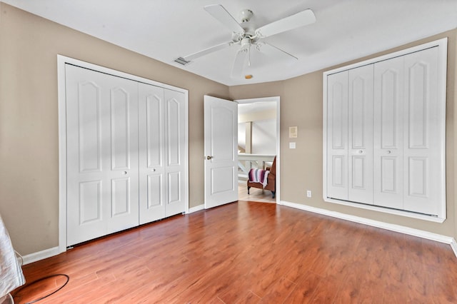 unfurnished bedroom featuring ceiling fan, multiple closets, and hardwood / wood-style flooring