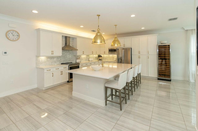 kitchen featuring wine cooler, appliances with stainless steel finishes, an island with sink, white cabinets, and wall chimney exhaust hood