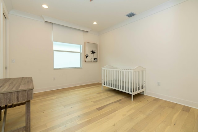 bedroom featuring crown molding, a crib, and light wood-type flooring