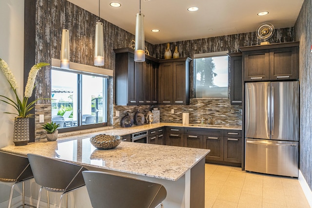 kitchen with kitchen peninsula, stainless steel fridge, light stone counters, and dark brown cabinetry