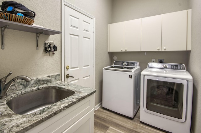 clothes washing area with cabinets, sink, separate washer and dryer, and light hardwood / wood-style floors