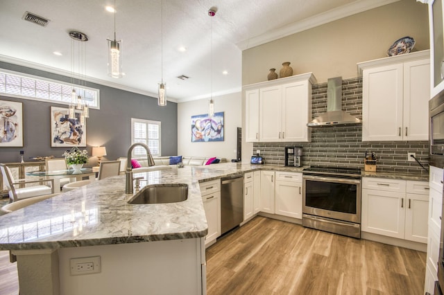 kitchen featuring white cabinetry, appliances with stainless steel finishes, pendant lighting, wall chimney exhaust hood, and sink