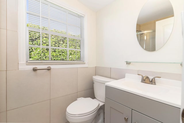 bathroom featuring vanity, toilet, tile walls, and a shower with shower door