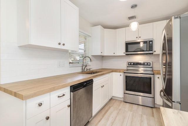 kitchen featuring stainless steel appliances, sink, white cabinets, hanging light fixtures, and butcher block counters