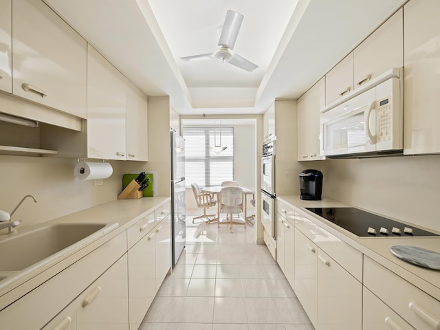 kitchen featuring ceiling fan, a raised ceiling, white appliances, light tile patterned flooring, and sink