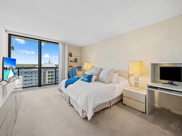 bedroom with a wall of windows, light colored carpet, and a textured ceiling