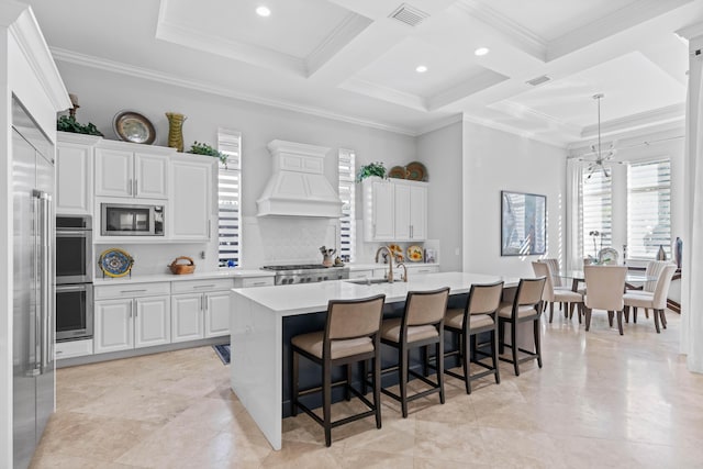 kitchen featuring built in appliances, a kitchen island with sink, white cabinets, and coffered ceiling