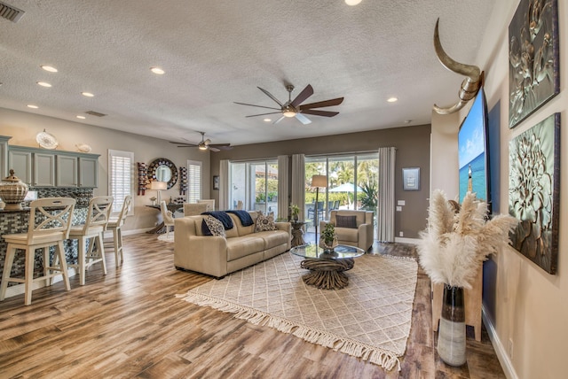 living room featuring light wood-type flooring, a textured ceiling, plenty of natural light, and ceiling fan