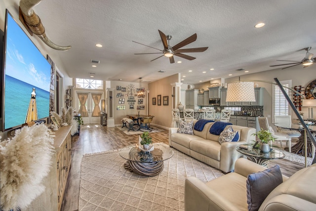 living room with light hardwood / wood-style flooring, ceiling fan with notable chandelier, and a textured ceiling