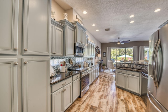 kitchen featuring ceiling fan, stainless steel appliances, dark stone countertops, a textured ceiling, and decorative backsplash