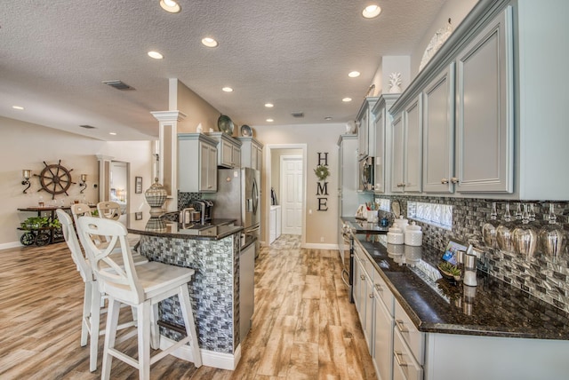 kitchen with gray cabinets, stainless steel appliances, light hardwood / wood-style floors, a kitchen bar, and decorative backsplash