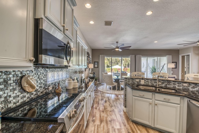 kitchen featuring appliances with stainless steel finishes, tasteful backsplash, sink, dark stone counters, and light hardwood / wood-style flooring