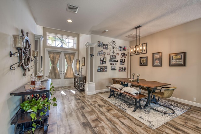 dining room with hardwood / wood-style floors, a notable chandelier, a textured ceiling, french doors, and ornate columns