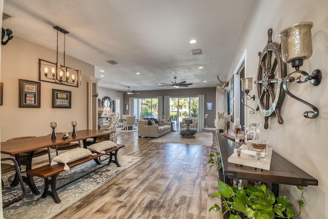 dining area with hardwood / wood-style flooring, ceiling fan with notable chandelier, and a textured ceiling