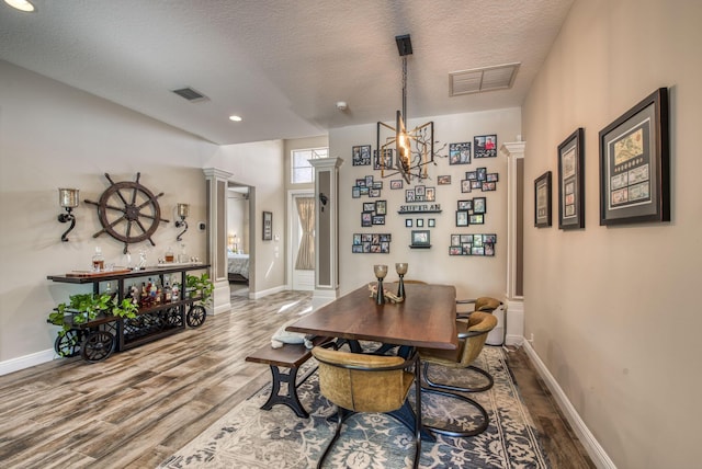 dining room featuring decorative columns, hardwood / wood-style floors, and a textured ceiling