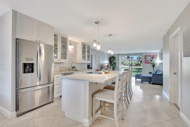 kitchen with stainless steel fridge, backsplash, a kitchen island, white cabinets, and a kitchen bar