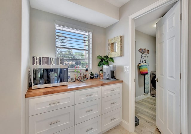 interior space with wooden counters, washer / dryer, light wood-type flooring, and white cabinets