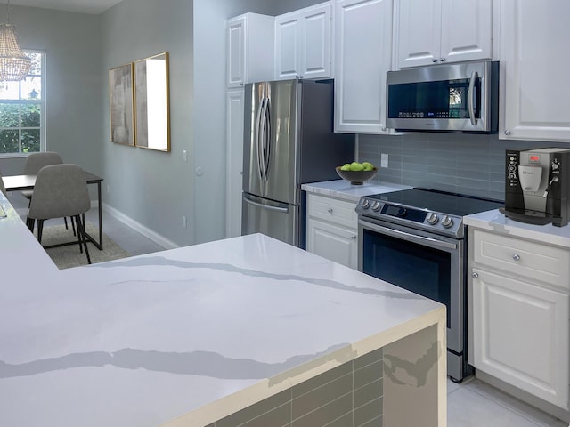 kitchen with pendant lighting, white cabinets, light stone countertops, tasteful backsplash, and stainless steel appliances