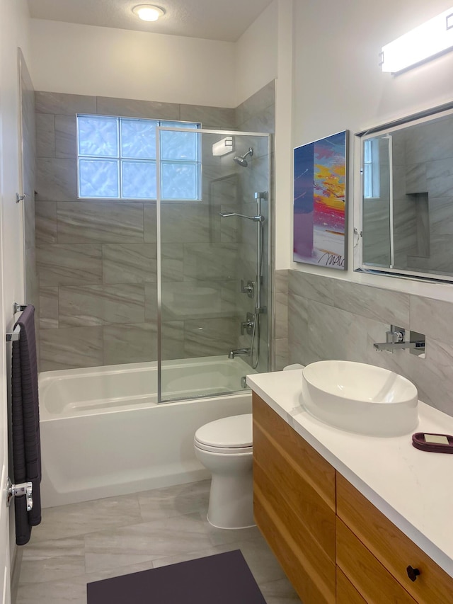 full bathroom featuring tile patterned flooring, combined bath / shower with glass door, toilet, vanity, and tile walls