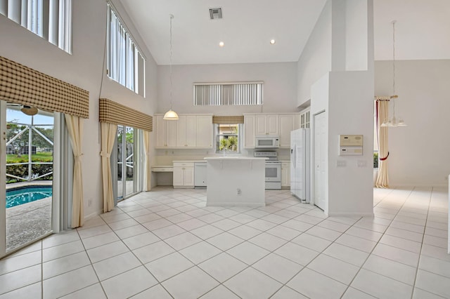 kitchen featuring white appliances, a center island, a towering ceiling, and light tile patterned flooring