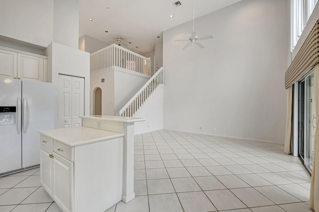 kitchen with light tile patterned flooring, a kitchen island, white fridge with ice dispenser, and a towering ceiling