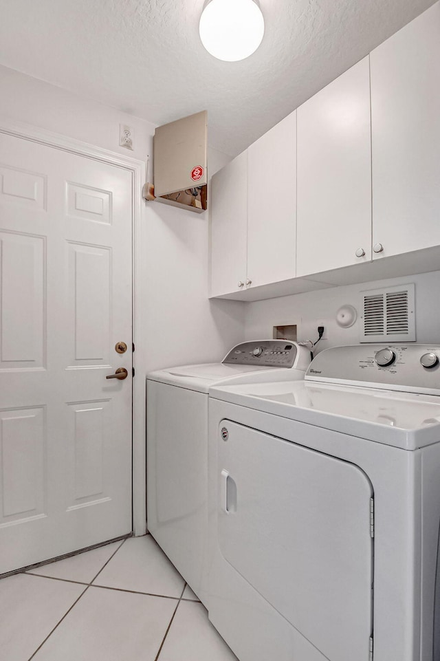 laundry room featuring cabinets, a textured ceiling, light tile patterned floors, and washing machine and dryer