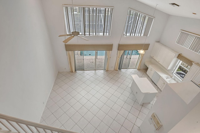 unfurnished living room with ceiling fan, a towering ceiling, and light tile patterned flooring