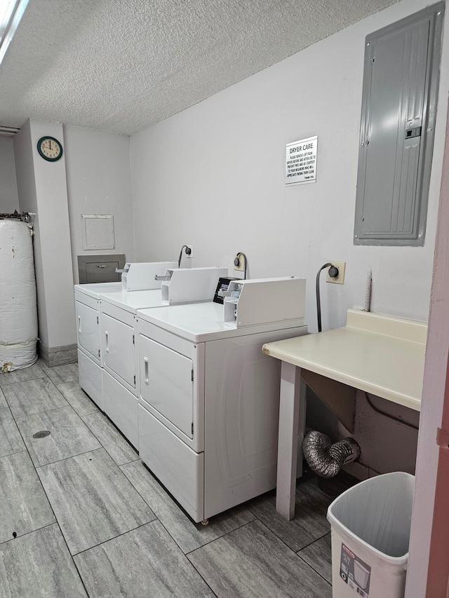 clothes washing area featuring washing machine and dryer, gas water heater, electric panel, and a textured ceiling