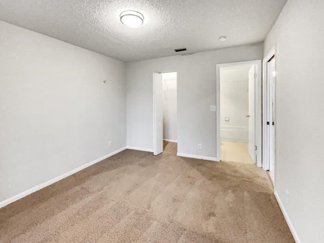 unfurnished bedroom featuring a walk in closet, a closet, light carpet, and a textured ceiling