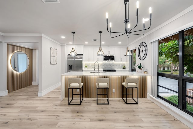 kitchen featuring a notable chandelier, backsplash, pendant lighting, white cabinets, and appliances with stainless steel finishes