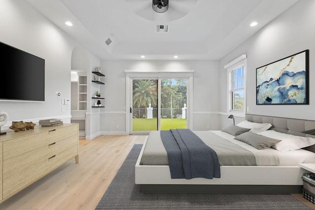 bedroom featuring ceiling fan, access to outside, light wood-type flooring, and a tray ceiling