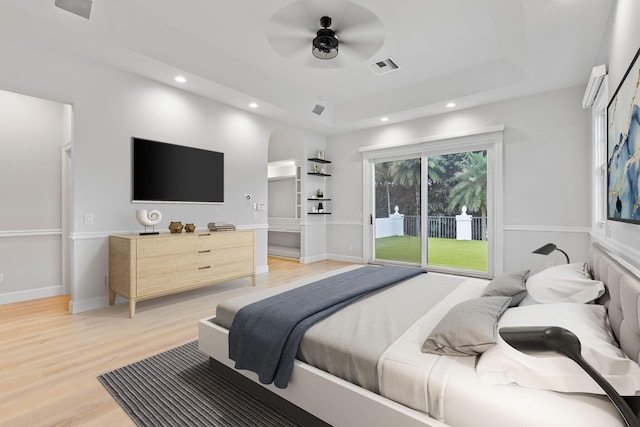 bedroom featuring ceiling fan, access to exterior, light hardwood / wood-style floors, and a tray ceiling