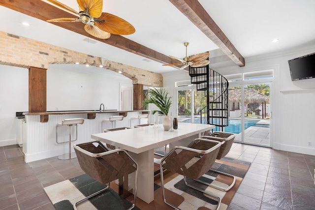 dining room with ceiling fan, brick wall, and beamed ceiling