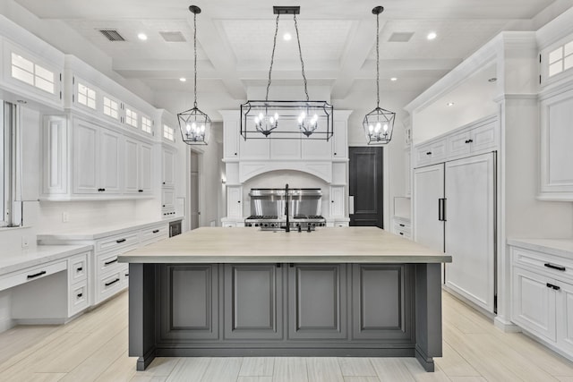 kitchen with beam ceiling, white cabinets, coffered ceiling, and a kitchen island with sink